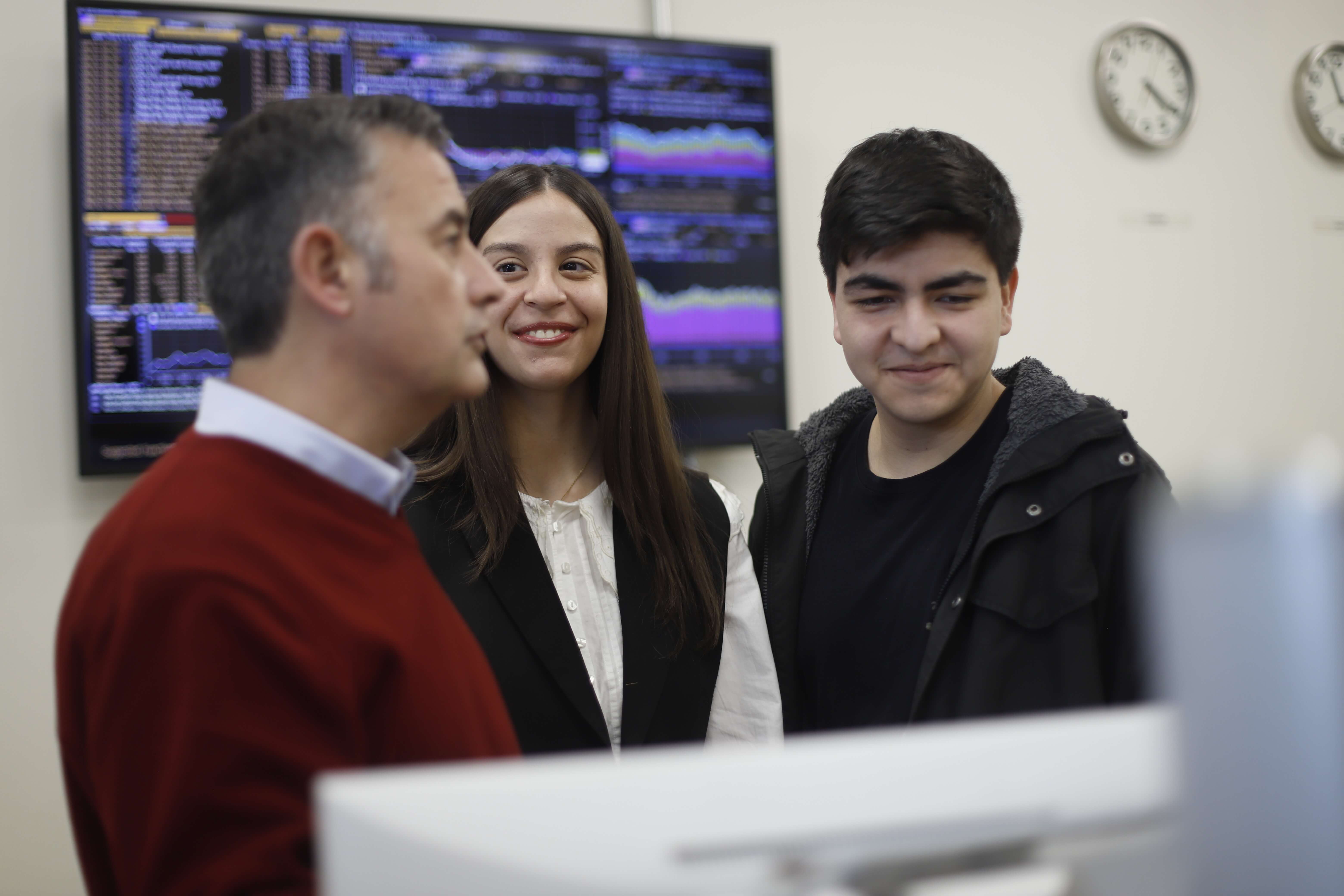 Estudiantes y profesor conversando frente a las pantallas del laboratorio de inversiones